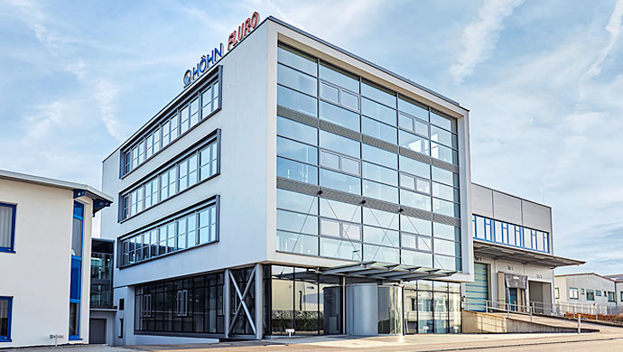 Modernes Gebäude mit großer Glasfront, oben sichtbar die Logos von HÖHN und FLURO