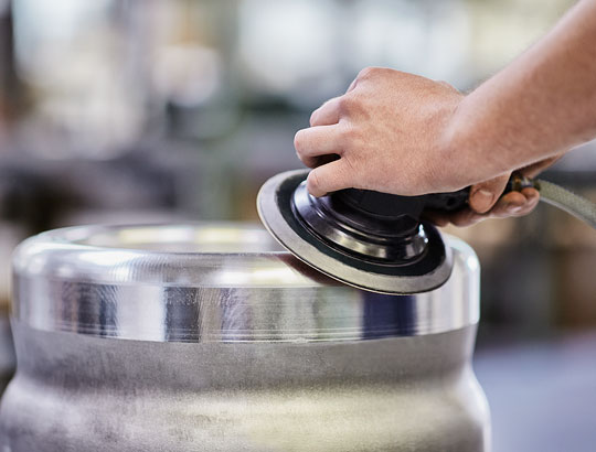 Hände führen Poliermaschine über eine Metalloberfläche – Veredelung und Glättung von Präzisionsteilen bei HÖHN