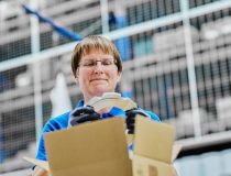 Frau legt ein Präzisionsteil sorgfältig in einen Karton und verpackt es für den Transport.